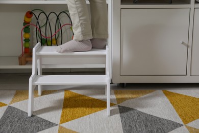 Photo of Little boy standing on step stool at home, closeup