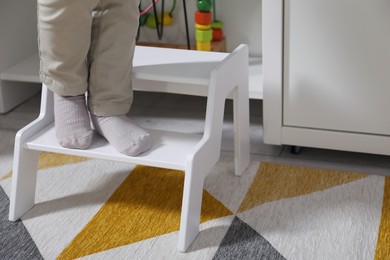 Photo of Little boy standing on step stool at home, closeup