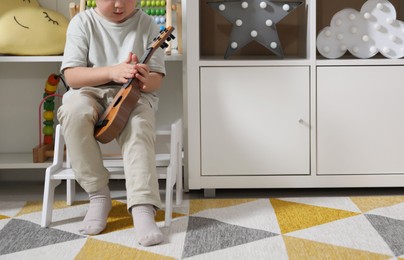 Little boy with toy guitar sitting on step stool at home