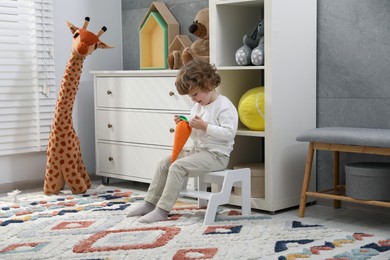 Little boy with toy sitting on step stool at home