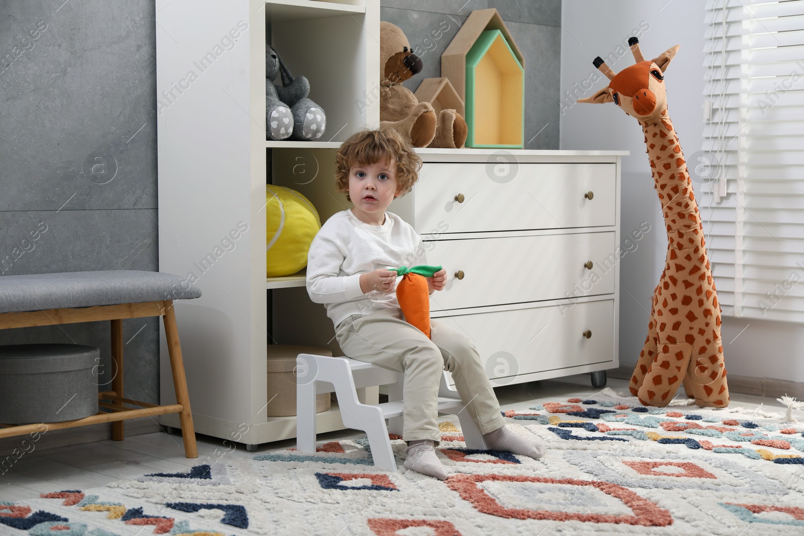 Photo of Little boy with toy sitting on step stool at home