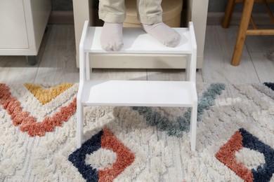 Photo of Little boy standing on step stool at home, closeup