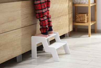 Little boy standing on step stool near bathroom vanity indoors, closeup