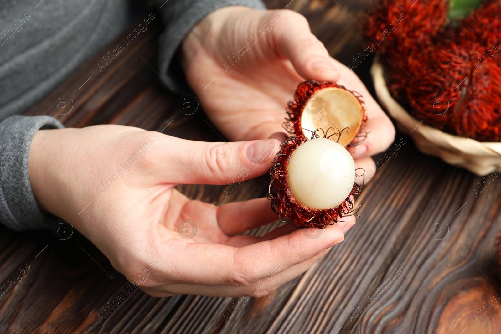 Photo of Woman peeling ripe rambutan at wooden table, closeup