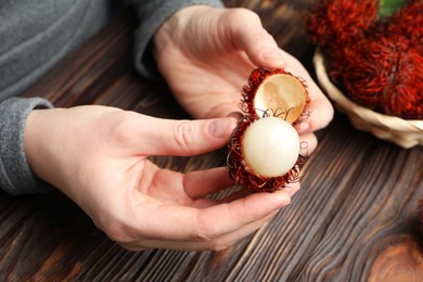 Woman peeling ripe rambutan at wooden table, closeup