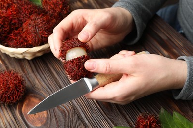 Photo of Woman peeling ripe rambutan at wooden table, closeup