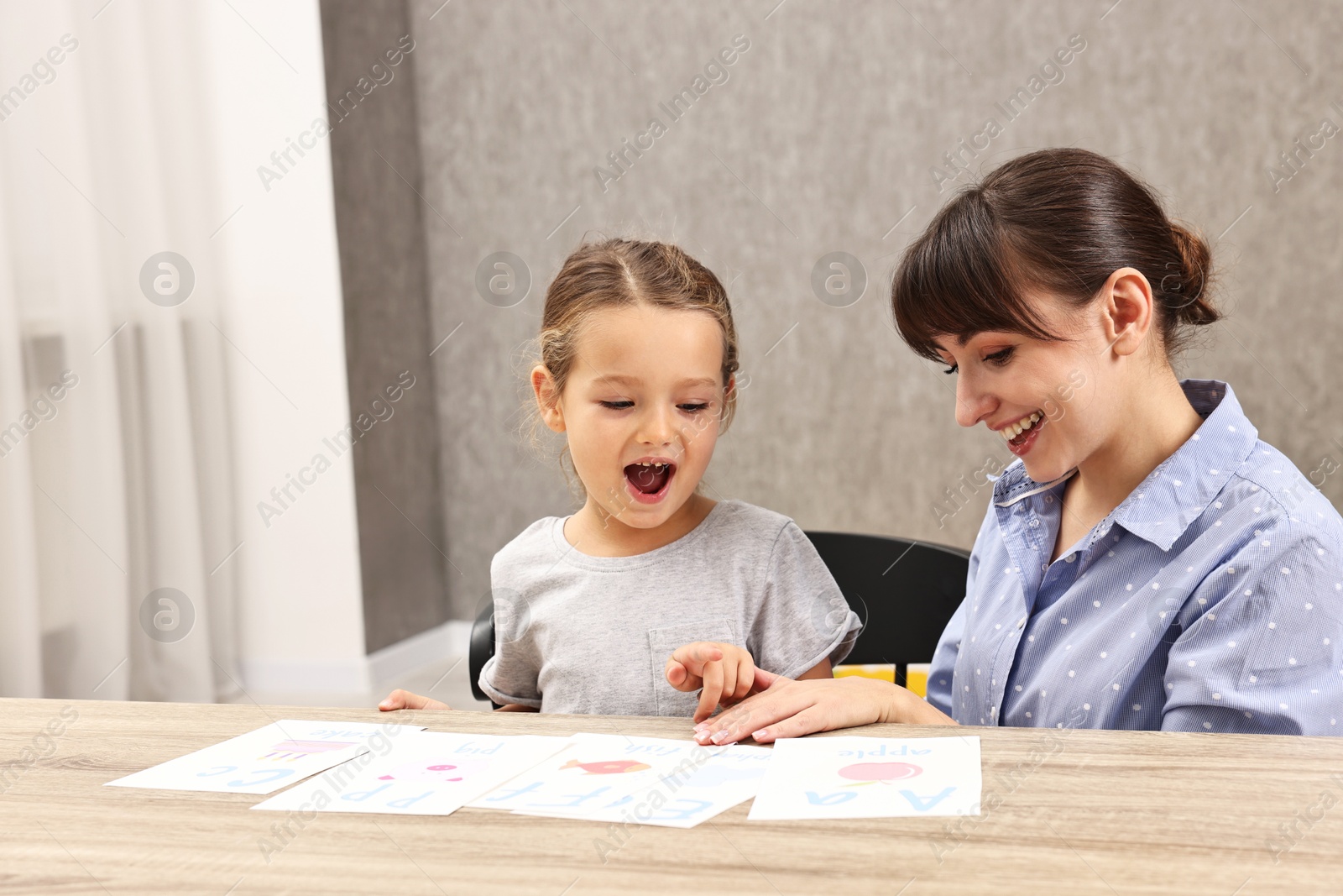 Photo of Smiling speech therapist working with little girl at table in autism treatment center. Space for text