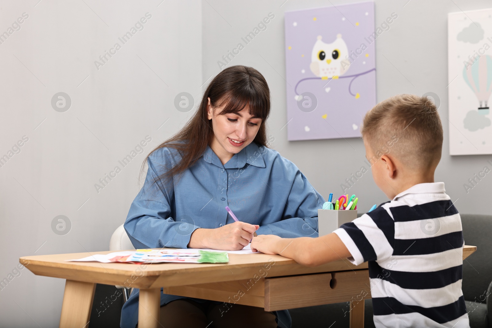 Photo of Autism therapy. Smiling psychologist and little boy drawing pictures at table in mental health center