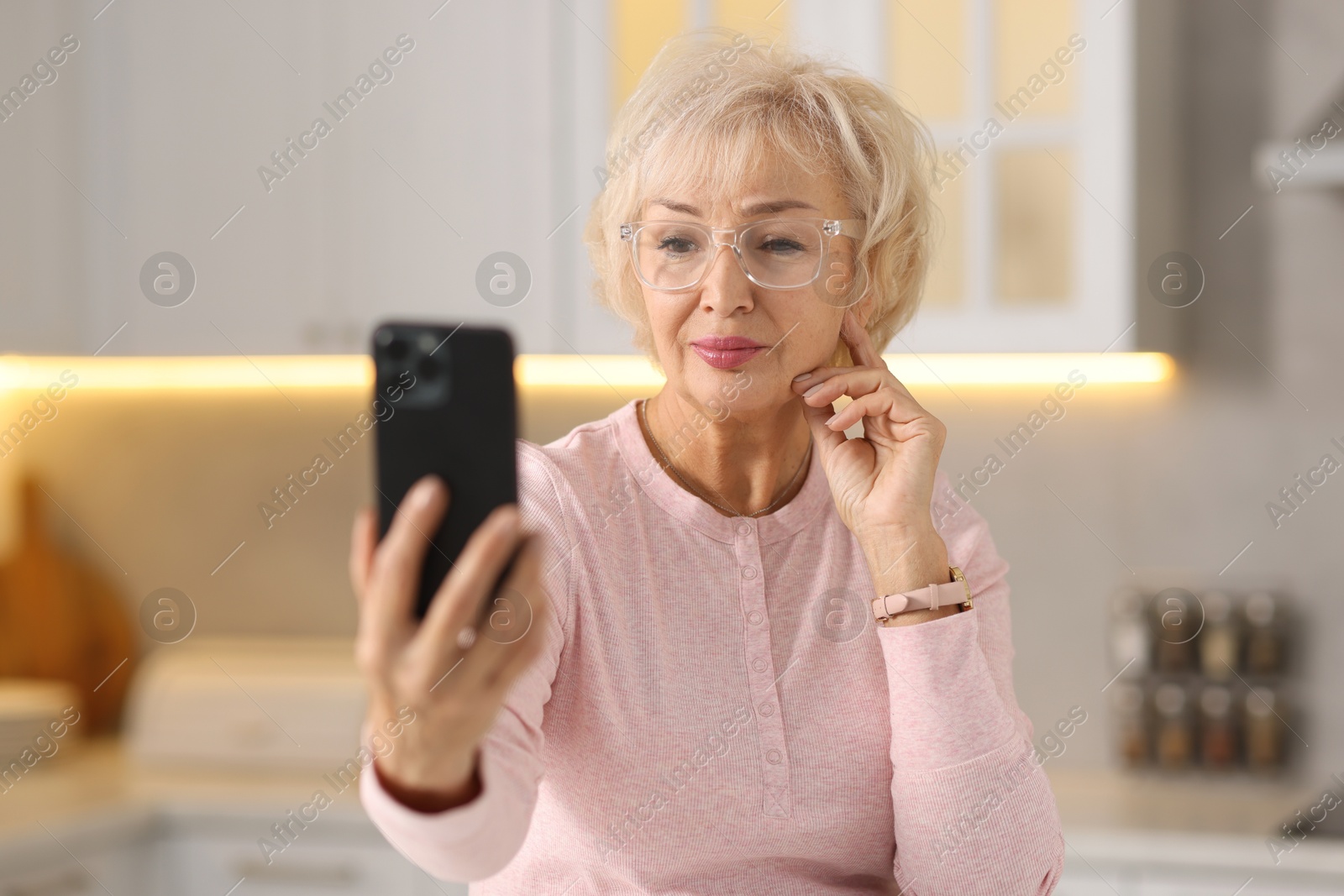 Photo of Beautiful grandmother using smartphone in kitchen, selective focus