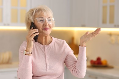 Photo of Beautiful grandmother talking on smartphone in kitchen