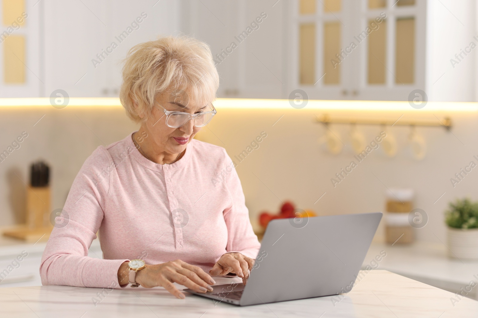 Photo of Beautiful grandmother using laptop at table in kitchen. Space for text