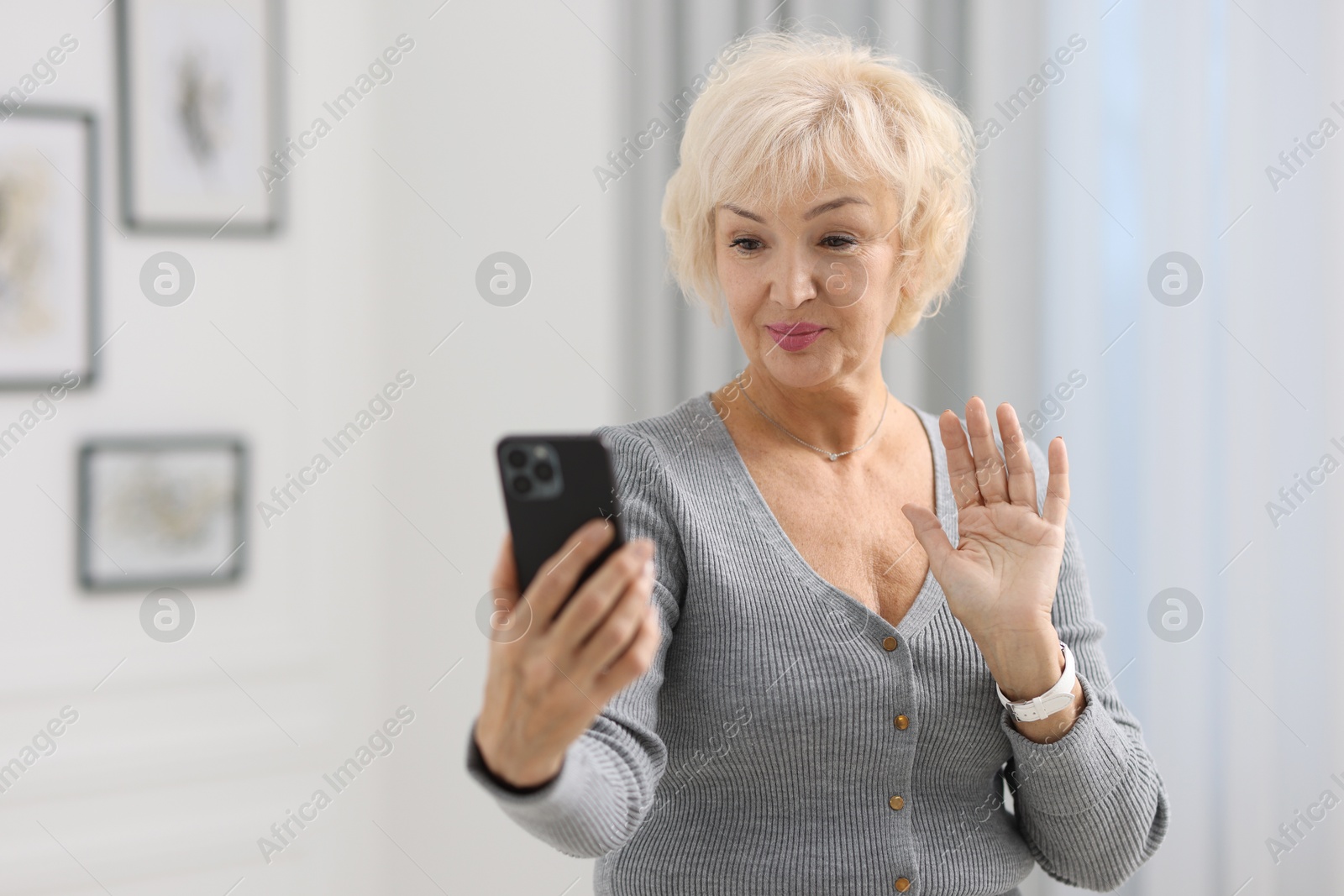 Photo of Beautiful grandmother having video chat via smartphone at home. Space for text