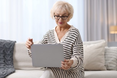 Photo of Beautiful grandmother using laptop on sofa at home