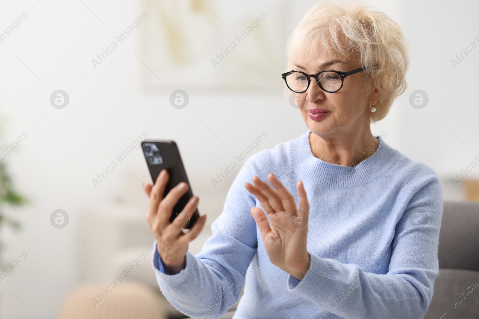 Photo of Beautiful grandmother in glasses using smartphone at home