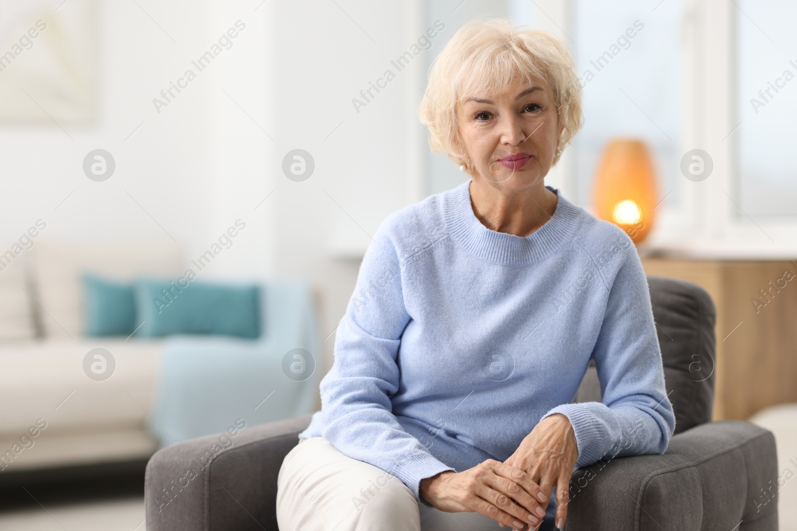 Photo of Beautiful grandmother sitting in armchair at home. Space for text