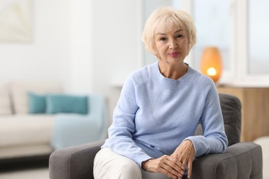 Beautiful grandmother sitting in armchair at home. Space for text