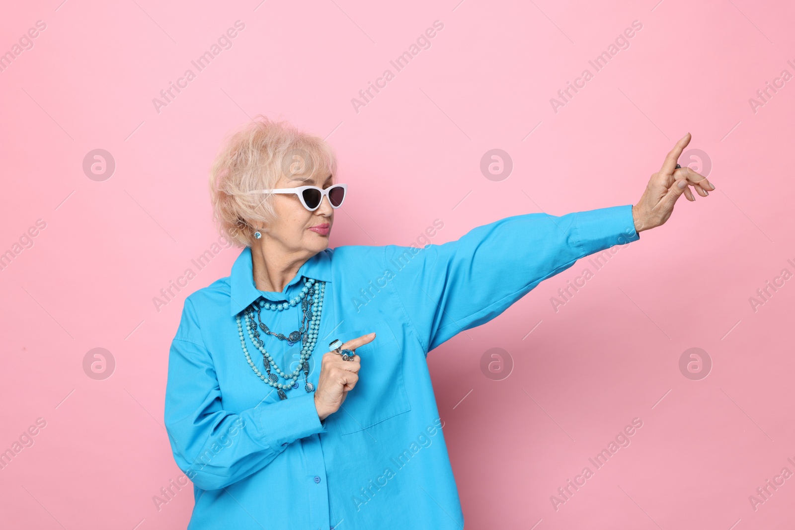 Photo of Portrait of cool grandmother in sunglasses on pink background