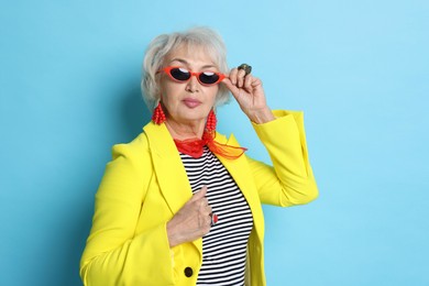 Photo of Portrait of fashionable grandmother in sunglasses and yellow jacket on light blue background