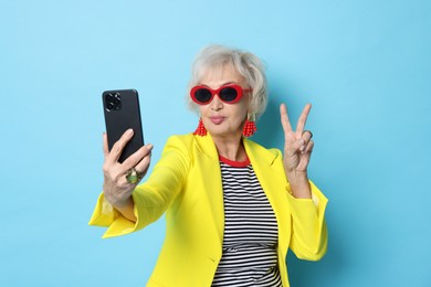 Cool grandmother showing V-sign while taking selfie on light blue background