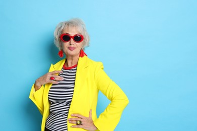 Portrait of fashionable grandmother in sunglasses and yellow jacket on light blue background. Space for text