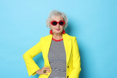 Photo of Portrait of fashionable grandmother in sunglasses and yellow jacket on light blue background