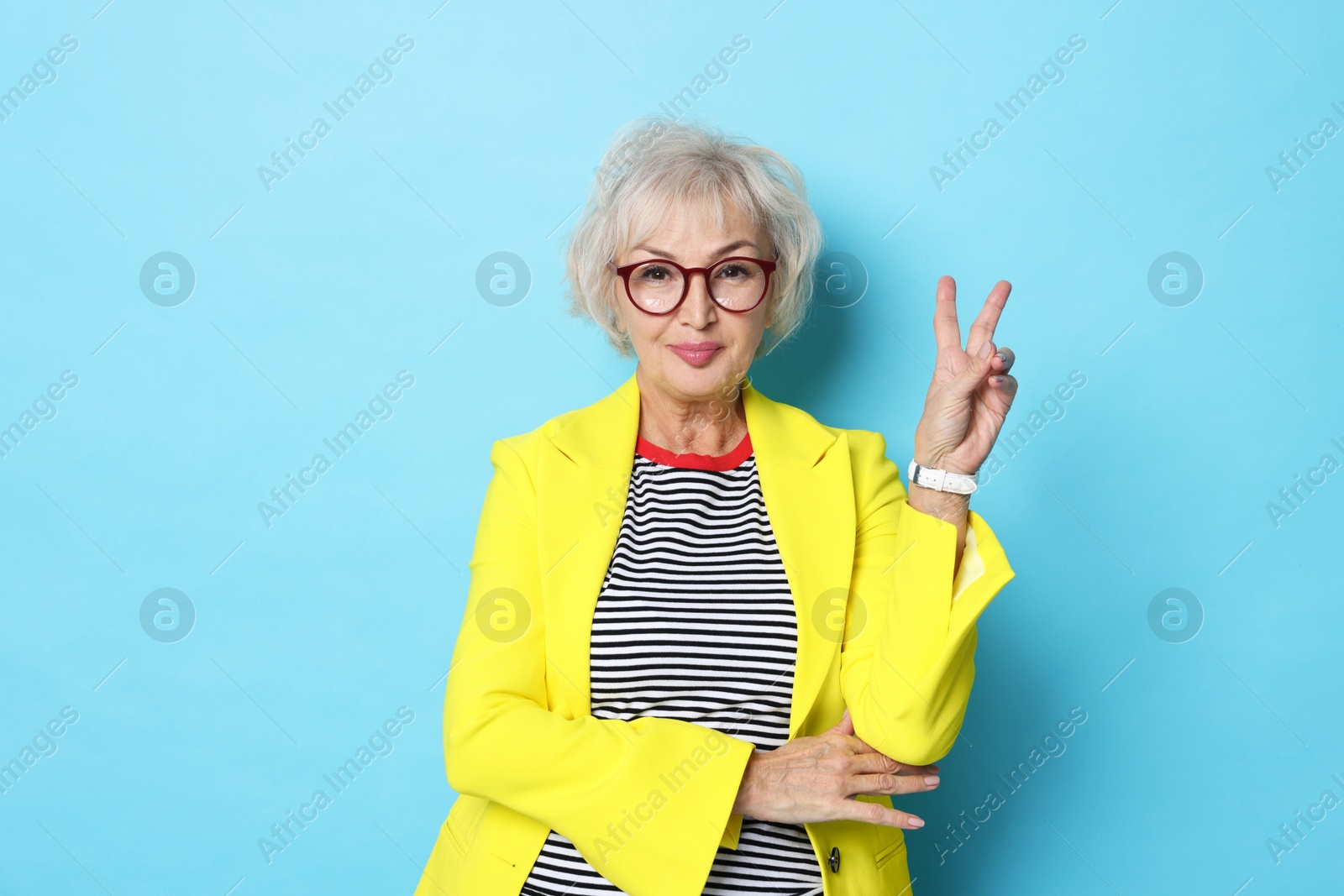 Photo of Portrait of fashionable grandmother in yellow jacket on light blue background