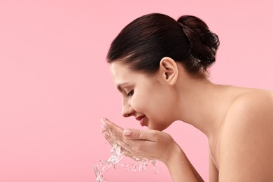 Photo of Attractive woman washing her face on pink background. Space for text