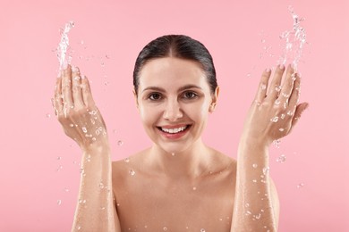 Smiling woman washing her face on pink background