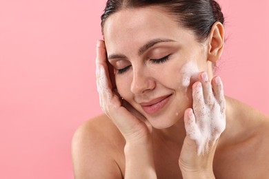 Photo of Attractive woman washing her face with cleansing foam on pink background, space for text