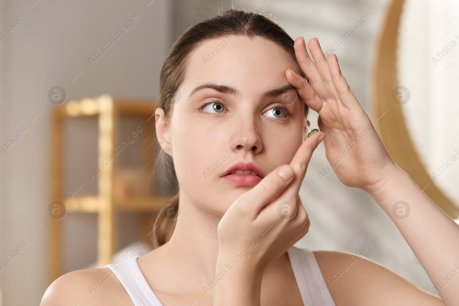 Photo of Young woman putting in green color contact lens indoors