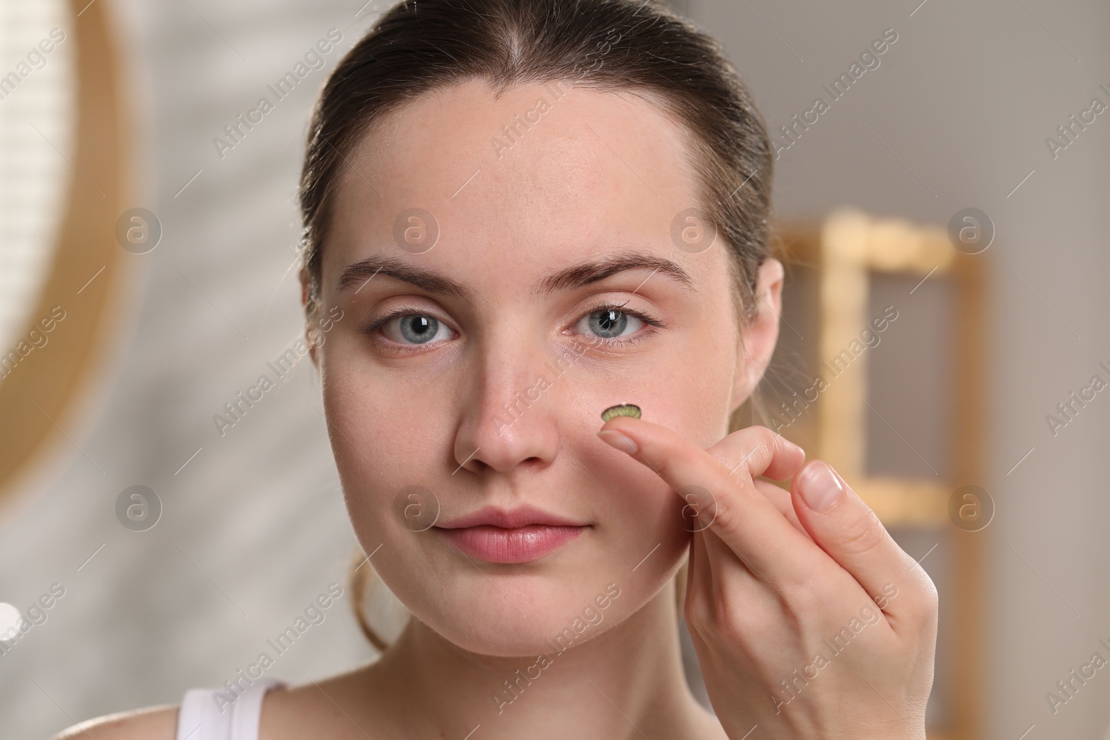 Photo of Young woman with green color contact lens indoors, closeup