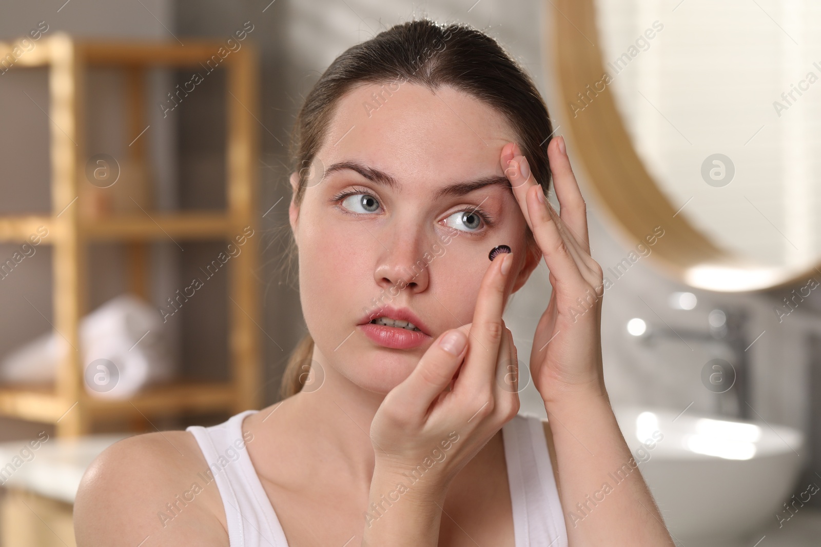 Photo of Young woman putting in color contact lens indoors