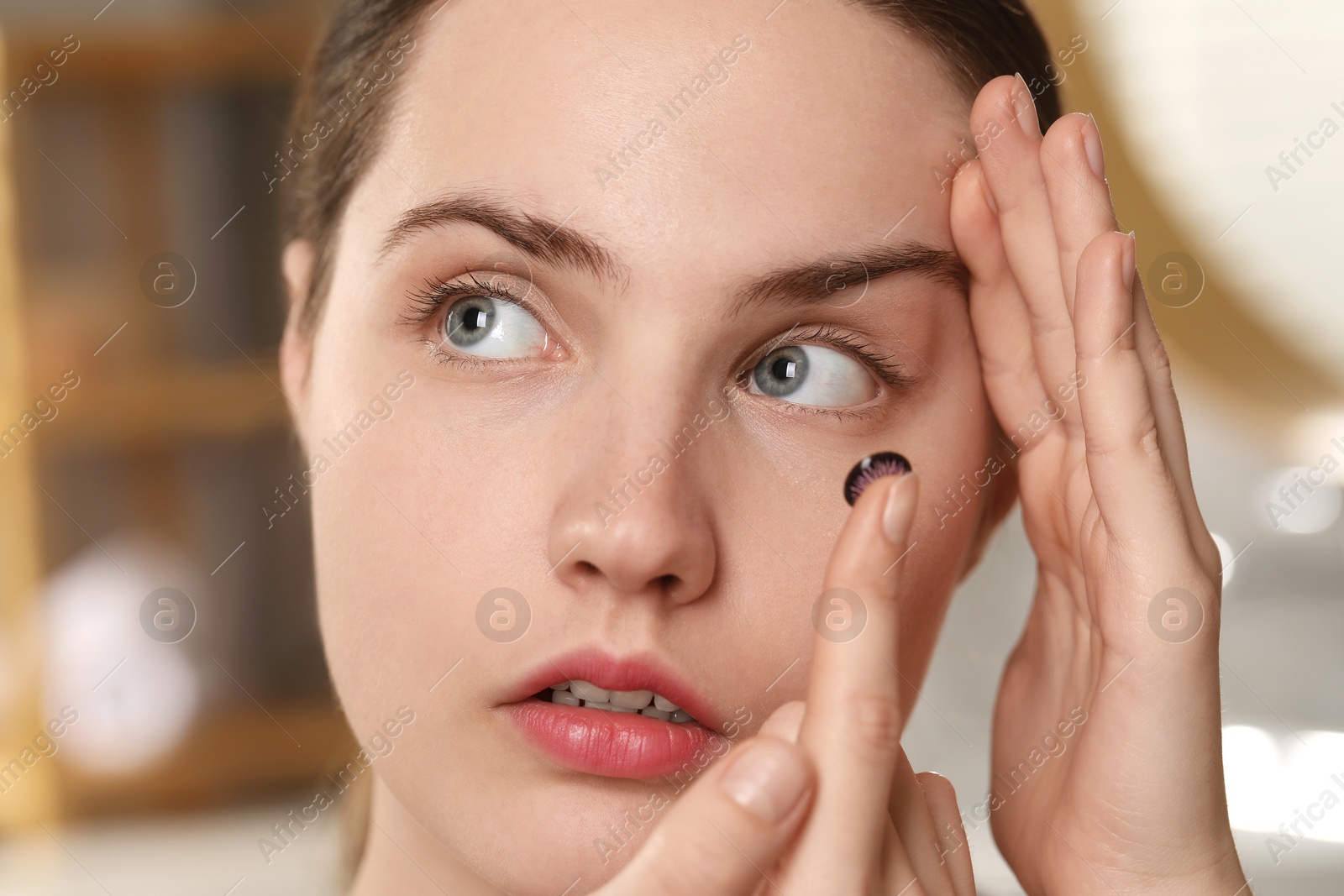 Photo of Young woman putting in color contact lens indoors, closeup