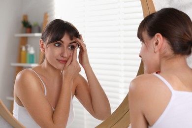 Young woman putting in color contact lens near mirror indoors