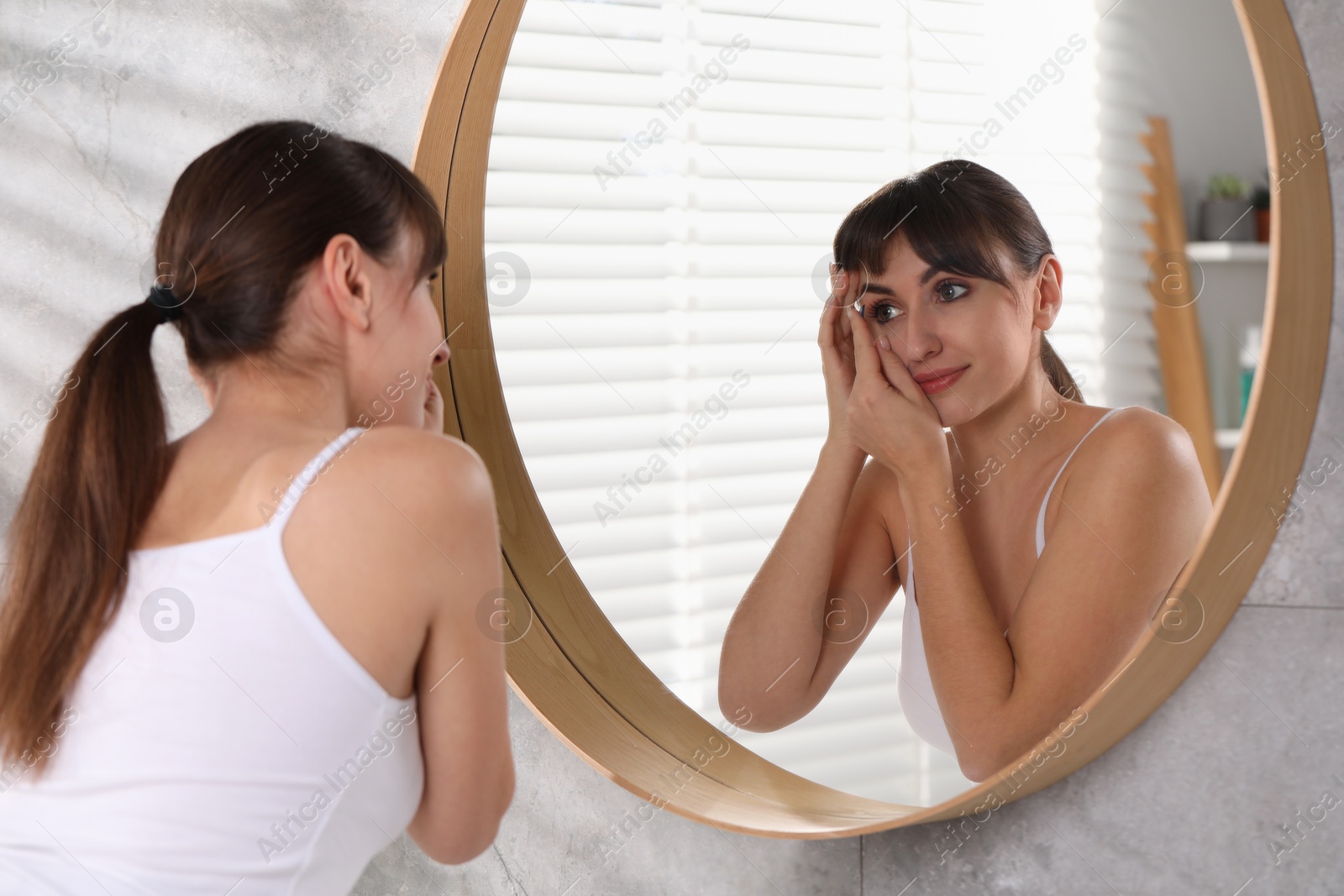 Photo of Young woman putting in color contact lens near mirror indoors