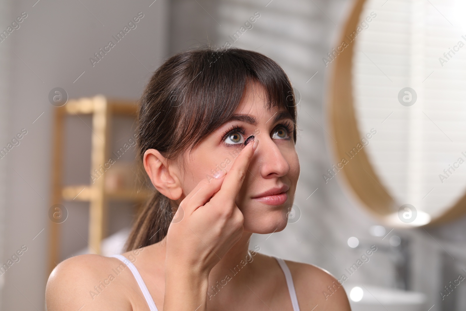 Photo of Young woman putting in color contact lens in bathroom