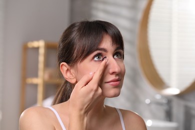 Young woman putting in color contact lens in bathroom