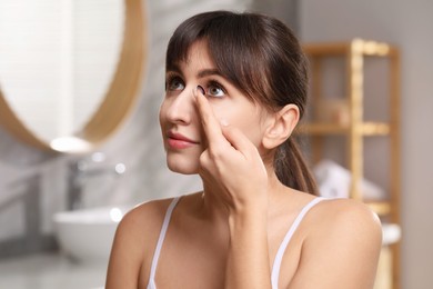 Photo of Young woman putting in color contact lens in bathroom