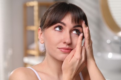 Young woman putting in color contact lens in bathroom