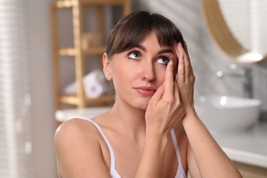 Young woman putting in color contact lens in bathroom