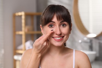 Photo of Young woman with color contact lens in bathroom