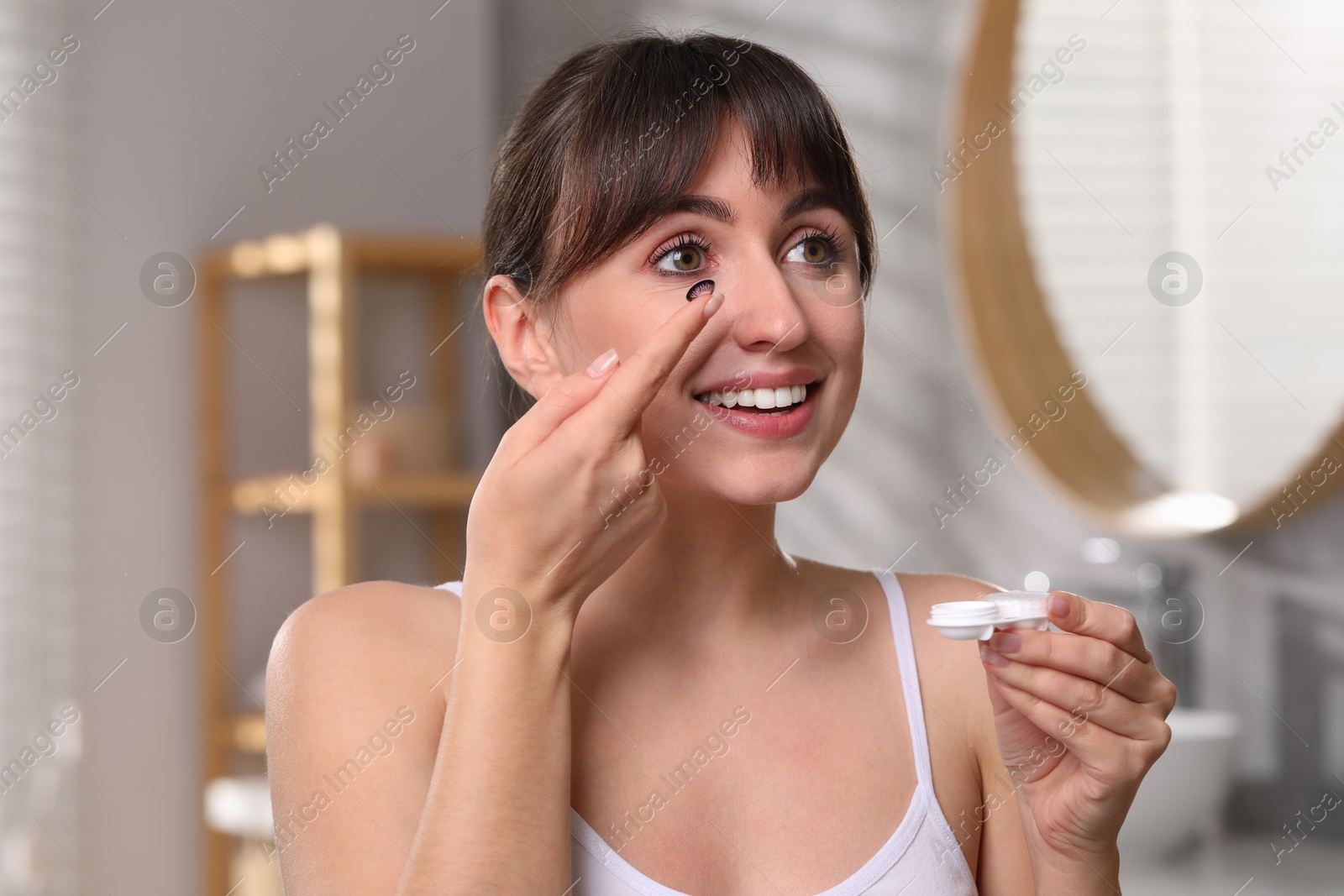 Photo of Young woman with color contact lens and case in bathroom