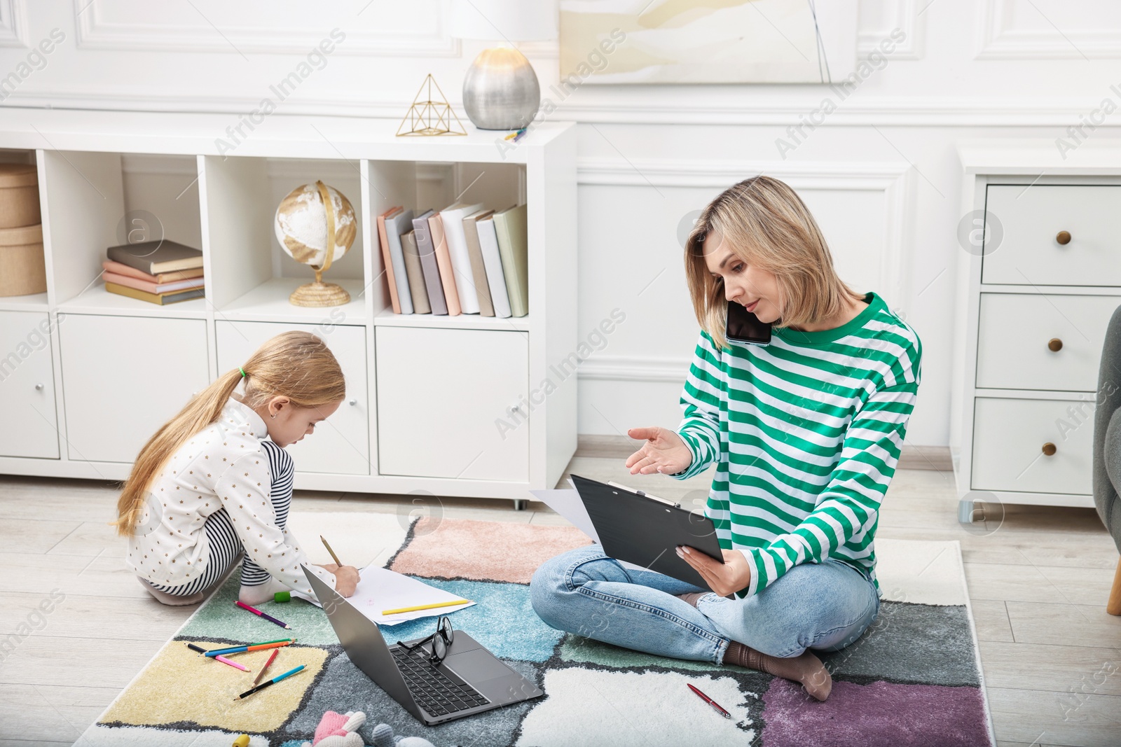 Photo of Work at home. Single mother talking by smartphone and her daughter drawing on floor indoors