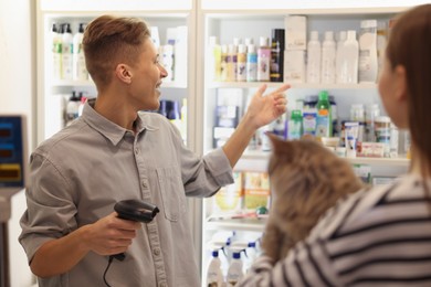 Photo of Cashier recommending cosmetic products to woman with cat in pet shop, selective focus