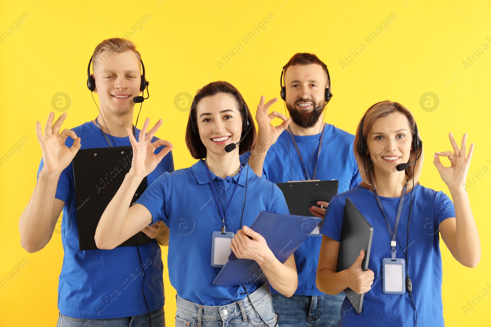 Photo of Technical support call center. Team of friendly operators showing ok gesture on yellow background