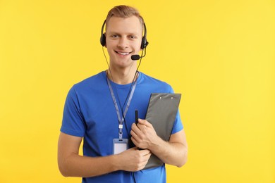 Photo of Technical support call center. Smiling operator with clipboard on yellow background