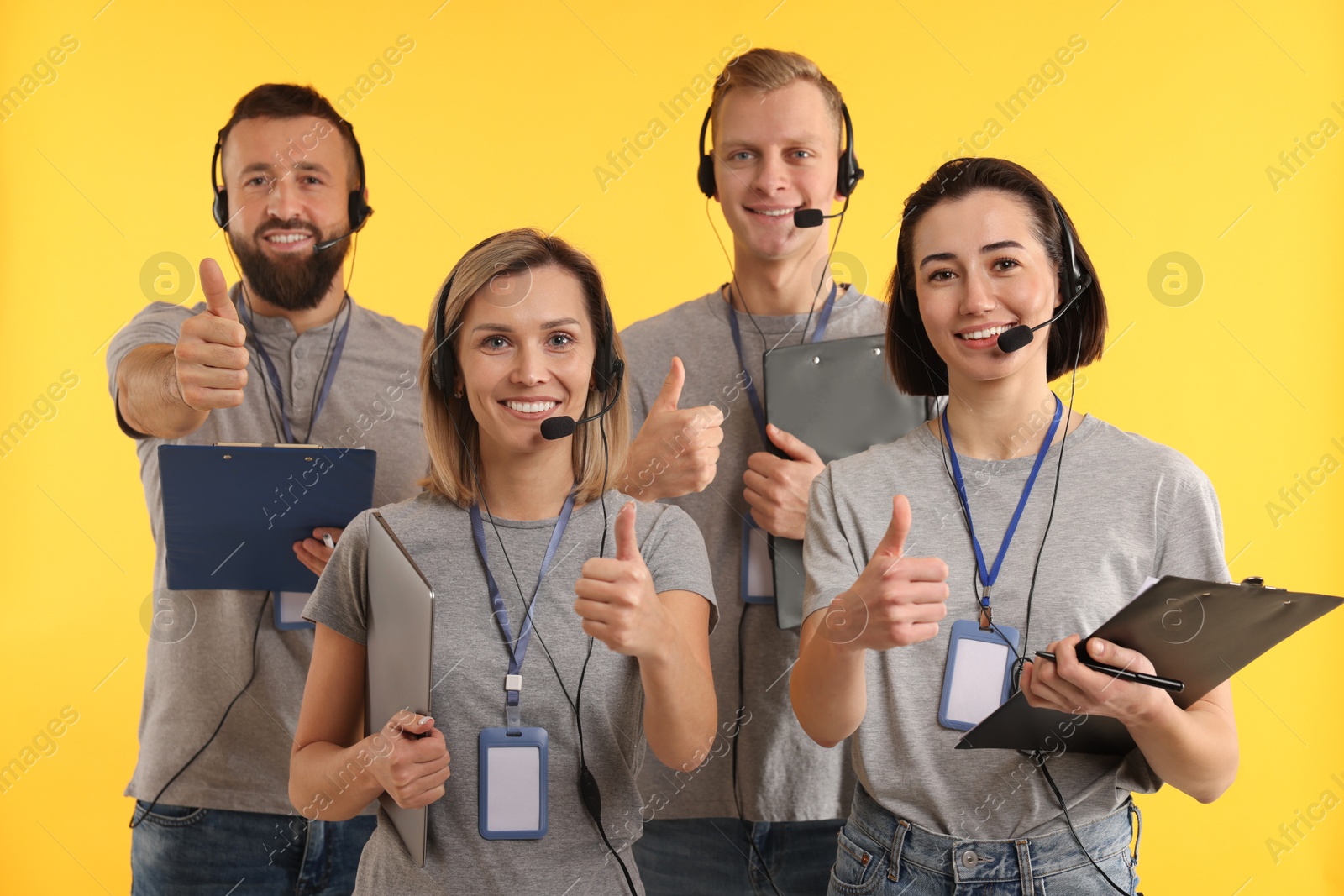 Photo of Technical support call center. Team of friendly operators showing thumbs up on yellow background