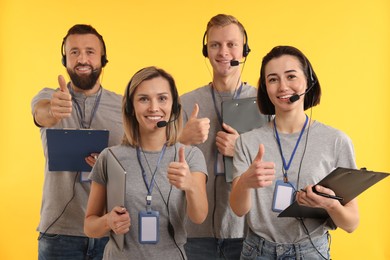 Technical support call center. Team of friendly operators showing thumbs up on yellow background