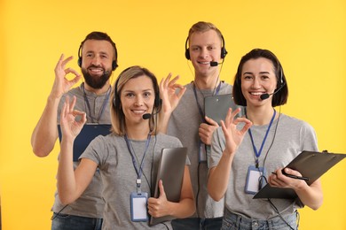 Photo of Technical support call center. Team of friendly operators showing ok gesture on yellow background