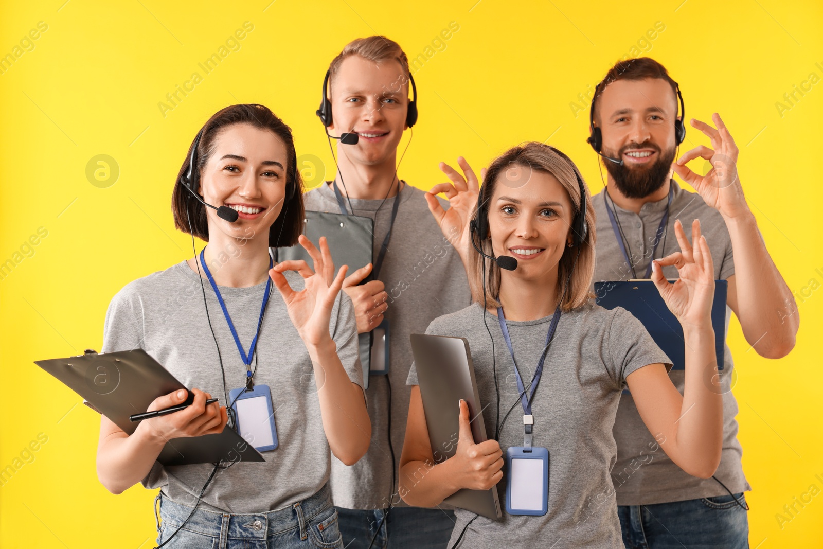 Photo of Technical support call center. Team of friendly operators showing ok gesture on yellow background